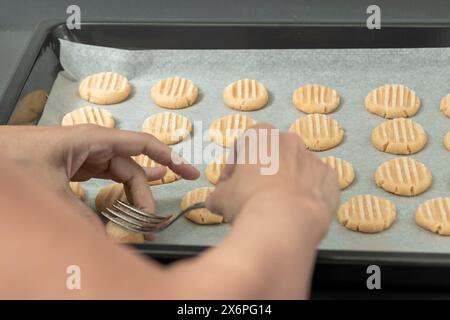 Eine Gabel in Teigkugeln auf einem Backblech drücken, um Muster auf ungebackenen Keksen zu erzeugen Stockfoto