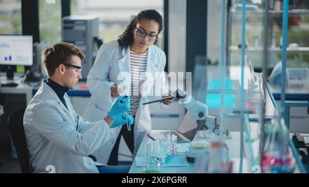 Modernes medizinisches Forschungslabor: Porträt zweier junger Wissenschaftler mit Pipette, Digital Tablet, Probenanalyse, Sprechen. Ein vielseitiges Team aus multiethnischen Spezialisten arbeitet im Advanced Lab Stockfoto