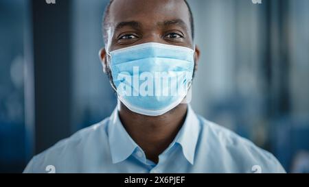 Nahaufnahme Porträt eines gutaussehenden schwarzen Afroamerikaners in weißem Hemd, der eine schützende Gesichtsmaske trägt. Erfolgreicher Mann, der ruhig in die Kamera schaut. Stilvoller Geschäftsmann oder Arzt im Krankenhaus. Stockfoto
