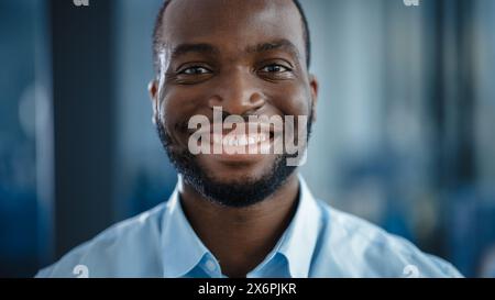 Nahaufnahme Porträt eines gutaussehenden Schwarzen Afroamerikaners in einem hellblauen Freizeitshirt. Erfolgreicher Mann lächelt ruhig, während er die Kamera ansieht. Glücklicher stilvoller Geschäftsmann oder Arzt im Krankenhaus. Stockfoto