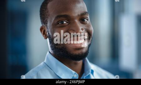 Nahaufnahme Porträt eines gutaussehenden Schwarzen Afroamerikaners in einem hellblauen Freizeitshirt. Erfolgreicher Mann lächelt ruhig, während er die Kamera ansieht. Glücklicher stilvoller Geschäftsmann oder Arzt im Krankenhaus. Stockfoto