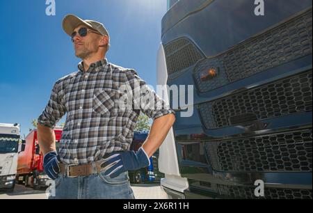 Kaukasischer Lkw-Fahrer in seinen 40ern, der an Sommertagen neben einem Lkw steht. Stockfoto
