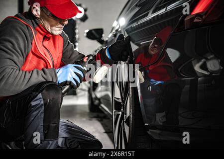 Ein Mann, der in einer Garage an einem Auto arbeitet. Karosserie polieren. Stockfoto