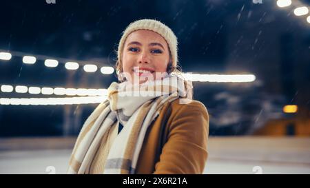 Winter Wonderland on Ice Rink: Point of View Porträt des schönen Mädchens Eislaufen mit Partner. Glückliche Lächelnde Frau. Ein Paar verliebt sich beim lustigen Tanz, Eiskunstlauf. Wunderschöne Schneefälle. POV-Aufnahme Stockfoto