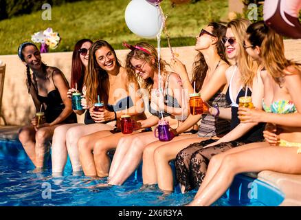 Gruppe von Freundinnen auf einer Sommerparty am Pool, die am Rand eines Swimmingpools sitzt und Spaß hat. Stockfoto