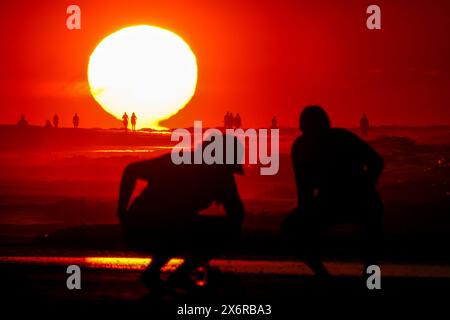 Isle Of Palms, Usa. Mai 2024. Menschen, die von einem dramatischen Sonnenaufgang umgeben sind, versammeln sich an einem klaren, heißen Tag am 16. Mai 2024 in Isle of Palms, South Carolina. Quelle: Richard Ellis/Richard Ellis/Alamy Live News Stockfoto