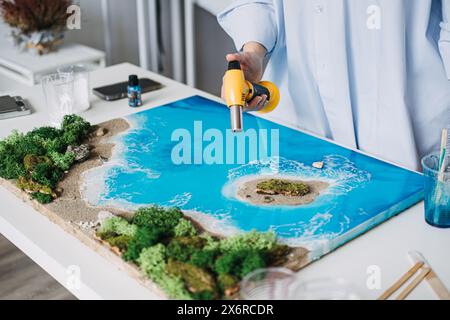 Künstler perfektionieren Epoxidharz Küstenszene mit Handbrenner Stockfoto