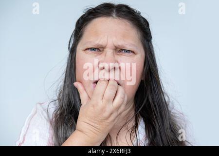 Die verzweifelte reife Frau mit langen Haaren, die nervös in die Nägel beißen, zeigt häusliche Gewalt Anzeichen von Angst und Trauma Stockfoto