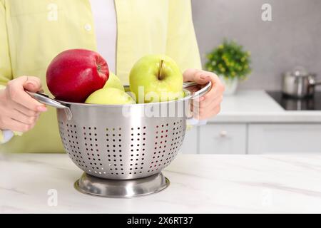 Frau, die ein Sieb mit frischen Äpfeln an einem weißen Marmortisch in der Küche hält, Nahaufnahme. Leerzeichen für Text Stockfoto