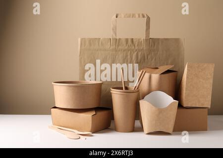 Umweltfreundliche Lebensmittelverpackungen. Papierbehälter, Geschirr und Tasche auf weißem Tisch vor beigefarbenem Hintergrund Stockfoto