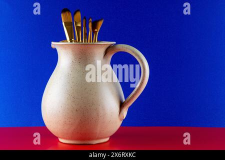 Künstler malen Pinsel in einem Weinkrug aus Steingut auf blauem Hintergrund und rotem Grund Stockfoto