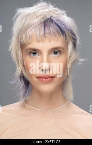 Nahporträt einer jungen Frau mit blondem und gefärbtem Haar, Septumpiercing und transparentem Oberteil. Moderne Frisur und Make-up, Mode Stockfoto