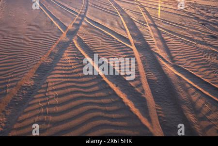 Perspektive der Reifenspuren am Sandstrand mit Sonnenuntergang Stockfoto