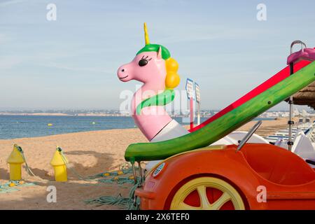 Tretboote am Strand. Einhorn in Pink mit rotem Auto und grüner Rutsche. Tretboot für Strand- und Strandunterhaltung. Stockfoto