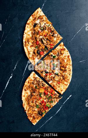 Gourmet-Pizzascheiben mit Gemüse und Huhn auf dunklem Hintergrund Stockfoto