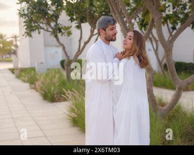 Reisen Sie in die Vereinigten Arabischen Emirate, Abu Dhabi. Arabisches Paar besucht den Park in der Nähe der Großen Moschee in Abu Dhabi in traditioneller Kleidung. Stockfoto