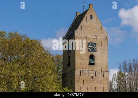 Ein mittelalterlicher Glockenturm mit Uhren auf beiden Seiten vor blauem Himmel, historische Häuser und eine Kirche mit kleinen Straßen und Laternen, Nes, Ameland Stockfoto