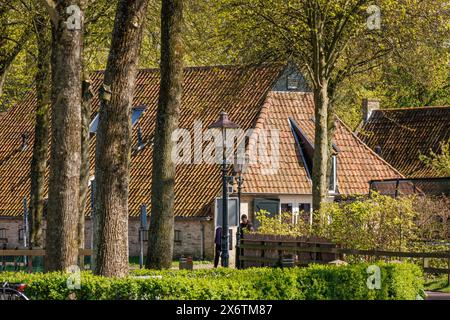 Ein Haus mit schrägem Dach und Laterne im Vordergrund, umgeben von hohen Bäumen im Frühjahr, historischen Häusern und einer Kirche mit kleinen Straßen und Stockfoto