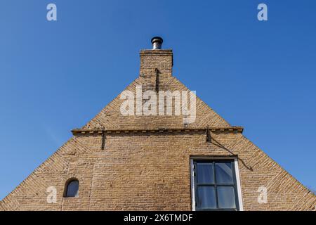 Backsteinhausfassade mit Kamin vor einem klaren blauen Himmel, minimalistisches Aussehen, historische Häuser in einem kleinen Dorf mit kleinen Straßen und Bäumen Stockfoto