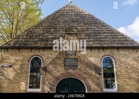 Traditionelles Backsteingebäude mit großem Dach, Fenstern und einem historischen Schild über dem Eingang, alten Häusern und kleinen Straßen mit Laternen und Grün Stockfoto