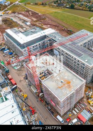 Große Baustelle mit mehreren Gebäuden im Bau, sichtbare Kräne und Fahrzeuge in ländlicher Umgebung, Baustelle eines neuen Stockfoto