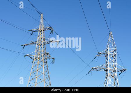 Hochspannungsmasten stehen hoch vor einem klaren blauen Himmel und tragen elektrische Kabel über die Landschaft. Stockfoto