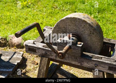 Eine abgenutzte Schleifscheibe sitzt auf einem rustikalen Holzständer, auf dem ein Metallhammer aufliegt und sich im Sonnenschein eines ruhigen Tages sonnt. Stockfoto