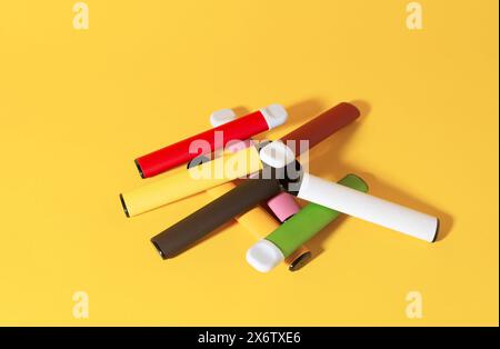 Layout farbenfroher elektronischer Einweg-Zigaretten mit Schatten auf gelbem Hintergrund. Das Konzept des modernen Rauchens, Vaping und Nikotin. Draufsicht Stockfoto