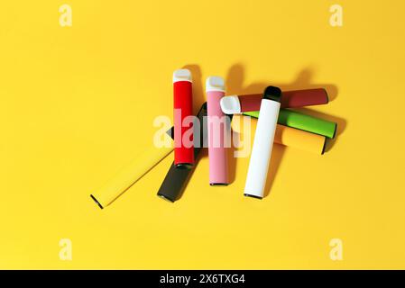 Layout farbenfroher elektronischer Einweg-Zigaretten mit Schatten auf gelbem Hintergrund. Das Konzept des modernen Rauchens, Vaping und Nikotin. Draufsicht. Stockfoto