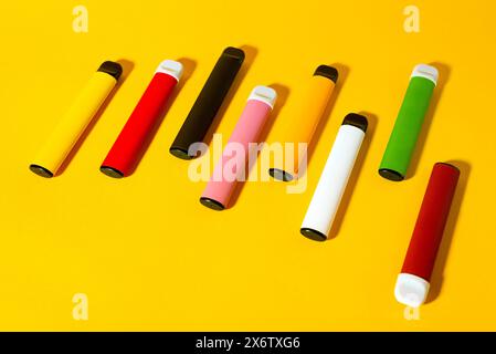 Layout farbenfroher elektronischer Einweg-Zigaretten mit Schatten auf gelbem Hintergrund. Das Konzept des modernen Rauchens, Vaping und Nikotin. Draufsicht. Stockfoto