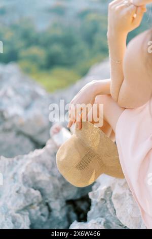 Eine junge Frau mit einem Hut in der Hand sitzt auf einem Felsen und legt ihr Kinn auf ihre Hand. Abgeschnitten Stockfoto