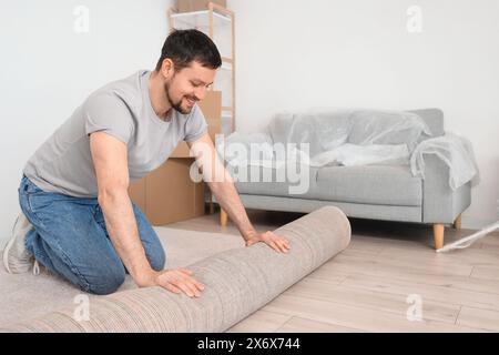 Junger Mann, der am Umzugstag Teppich im Zimmer ausrollt Stockfoto