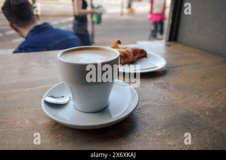 Eine Nahaufnahme einer dampfenden Tasse Kaffee in einer weißen Tasse mit Untertasse, die auf einem Holztisch in einem gemütlichen Café serviert wird. Stockfoto