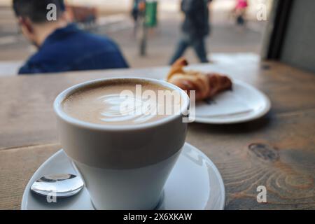 Eine Nahaufnahme einer dampfenden Tasse Kaffee in einer weißen Tasse mit Untertasse, die auf einem Holztisch in einem gemütlichen Café serviert wird. Stockfoto