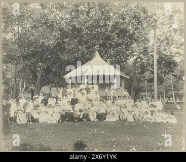 Gruppenporträt, Gruppenfoto einer großen Gruppe mit hauptsächlich Erwachsenen auf der linken und Kindern auf der rechten Seite. Posiert auf einem Rasen vor einer Kuppel mit einem Holzgiebeldach. Der Karton, auf dem das Foto geklebt ist, ist mit Blumen verziert. Wahrscheinlich ein Treffen anlässlich der Abreise von Banka Zinnbergbau Chef Robert Julius Boers in die Niederlande 1919., Foto, anonym, Bangka, 1919, fotografischer Träger, Höhe, 240 mm x Breite, 295 mm, Höhe, 342 mm x Breite, 418 mm Stockfoto