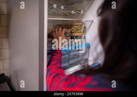 Indonesischer beschnittener Körper eines jungen Mädchens spielt und kocht, während er etwas im Kühlschrank zu Hause mitnimmt. Unterhaltsames Lernen für Hausarbeit und Kreativität Stockfoto