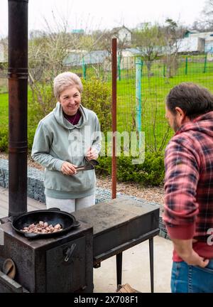 Reifer russischer Mann und Frau, die Fleisch in einem Kessel auf dem Herd im Freien braten, Familienkonzept Stockfoto