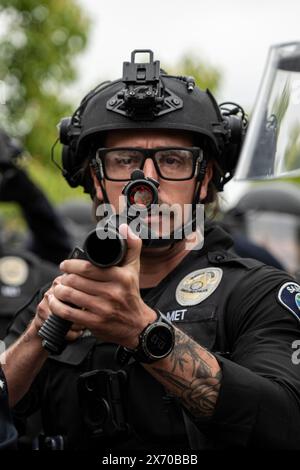 Irvine, Kalifornien, USA. Januar 2023. Ein Polizeibeamter von Santa Ana richtet seine nicht-tödliche Bean Bag-Waffe auf die Menge der Demonstranten, während sie auf das Lager vordringen. Beamte zahlreicher Polizeibehörden im Orange County, Kalifornien, wurden auf den Campus der University of California (UC) Irvine gerufen, um ein wachsendes palästinensisches Lager zu räumen, das das Zentrum der Universität übernahm. Die Studenten verbarrikadierten sich in einen Kreis und befestigten ihren Umkreis mit Holzpaletten und anderen Gegenständen, um die Behörden fernzuhalten. Insgesamt wurden 50 Demonstranten mit der e verhaftet Stockfoto