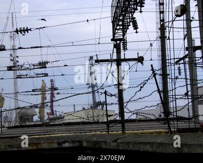 Foto von urbanen Details. Elektrische Pole und Drähte. Im Hintergrund sind Himmel, Gebäude, Baukräne. Vogelfliegen, Stacheldraht. Der Himmel ist bewölkt, gloo Stockfoto