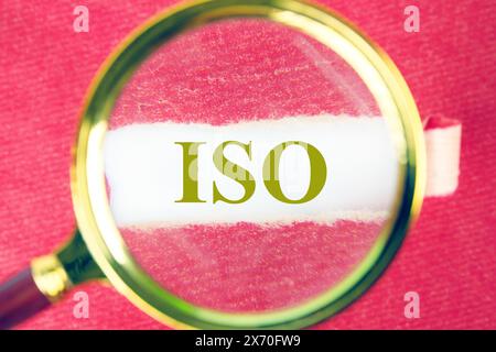 ISO. Internationale Organisation für Normung. Ein Wort ISO durch eine Lupe unter einem Stück zerrissenem Papier Stockfoto