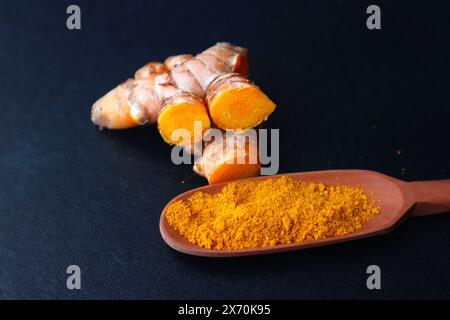 Kurkuma oder (Curcuma longa Linn) und Kurkumapulver in einem Holzlöffel auf dunklem Hintergrund. Stockfoto