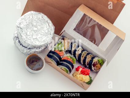 Sushi-Set auf einem weißen Tisch, Blick von oben, Behälter mit warmen Speisen in Folie und Sushi Stockfoto