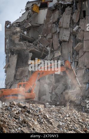 Ein Bagger zerstört aktiv ein altes Gebäude und schafft eine Szene aus Schutt und Staub. Der Vernichtungsprozess wird in Aktion erfasst. Stockfoto