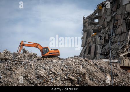 Ein Bagger an einer Abbruchstelle mit einem großen Schutt- und Schutthaufen neben einem teilweise abgerissenen Gebäude. Stockfoto