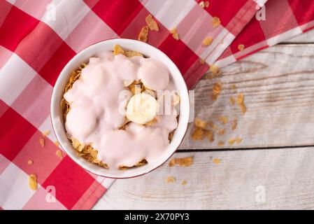 Gesundes Frühstück. Müsli mit Joghurt und Banane auf hellem Holzhintergrund mit roter Tischdecke. Blick von oben. Kopierbereich Stockfoto