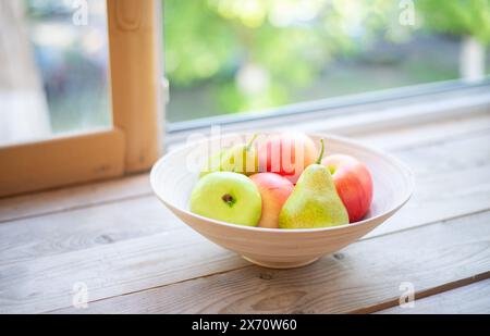 Äpfel und Birnen auf einer Fensterbank in einem Holzteller. Sommer und frisches Obst. Stockfoto