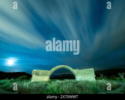 Langzeitbelichtungslandschaft der Brückenruine mit Reflexion des fließenden Wolkenhimmels bei Nacht Stockfoto