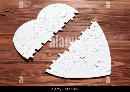 Eine Nahaufnahme eines weißen, herzförmigen Puzzles, das auf einem dunklen Holzhintergrund zerlegt liegt. Liebe, Verlust und die Suche nach Vollendung. Stockfoto