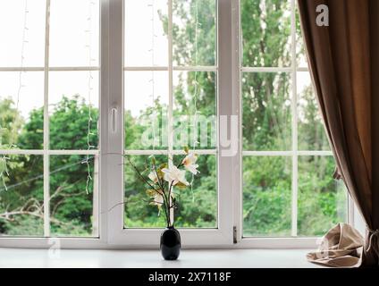 Eine Vase wunderschöner einsamer Blumen auf der Fensterbank im Raum, Platz für Text. Vorhänge und ein großes Fenster. Grüner Hintergrund. Stockfoto