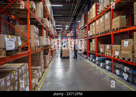 Lagerinnenraum des Vertriebszentrums mit Arbeiter, der Kartons auf den Gabelstapler verladet. Stockfoto